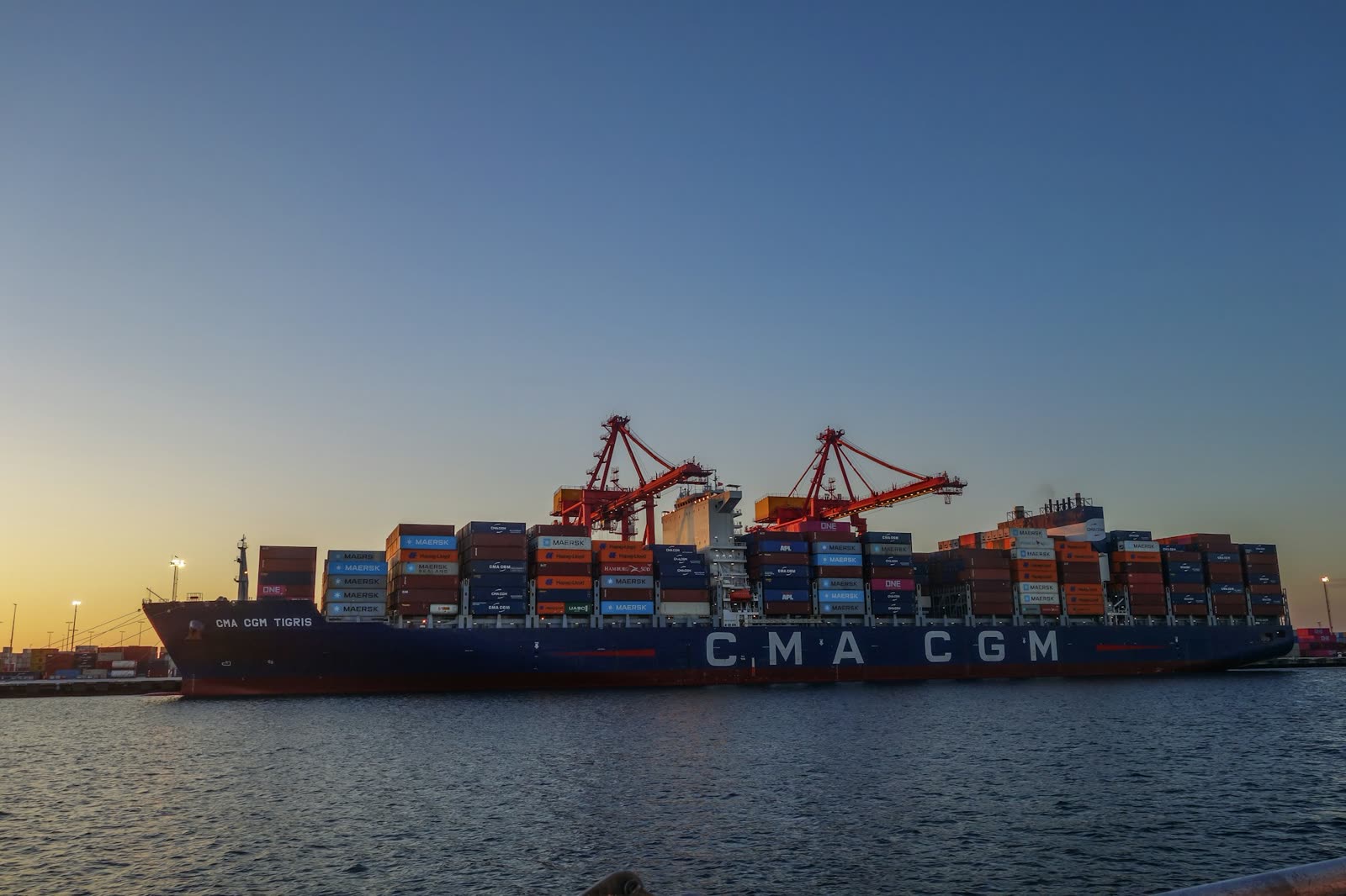 A container vessel with CMA CGM on its hull, alongside at dusk.