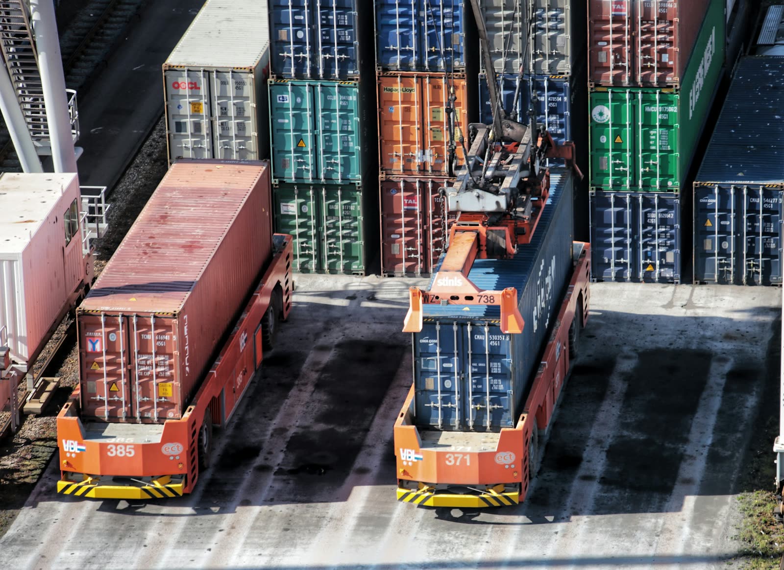 Stacked containers and two straddle carriers at a container terminal, seen from above.